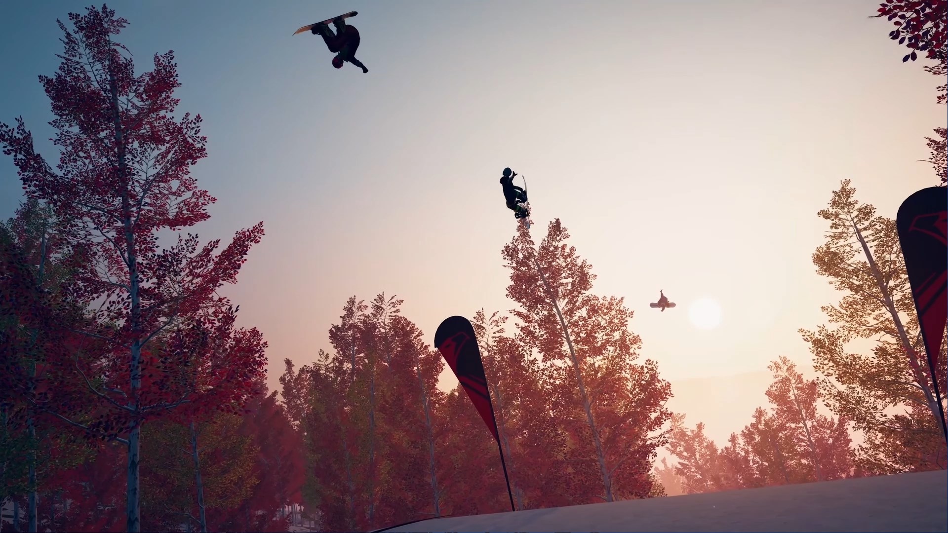 A group of snowboarders jump through the air at sunset, surrounded by trees